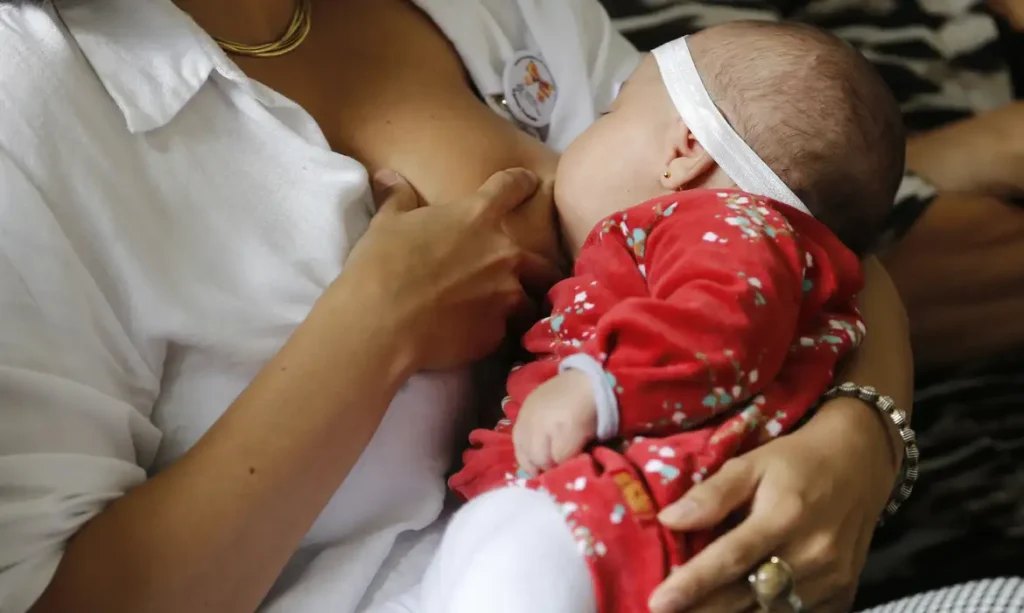 Mulher amamentando um bebê que usa uma roupa vermelha | Amamentar mais de um ano reduz risco de câncer de mama | NatureSoul